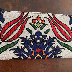 Puede incluir: Una bolsa blanca con cremallera con un estampado floral colorido. El estampado presenta flores rojas, azules, verdes y naranjas sobre un fondo blanco.