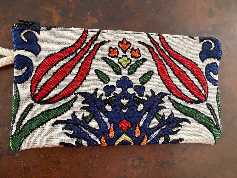 Puede incluir: Una bolsa blanca con cremallera con un estampado floral colorido. El estampado presenta flores rojas, azules, verdes y naranjas sobre un fondo blanco.