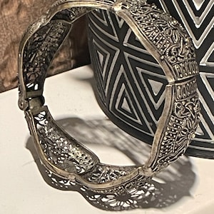 May include: A silver filigree bracelet with intricate floral designs. The bracelet is open and has a hinged clasp.