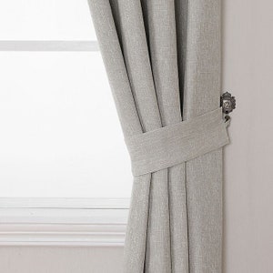 May include: A gray linen curtain with a fabric tieback and a decorative metal curtain holdback.