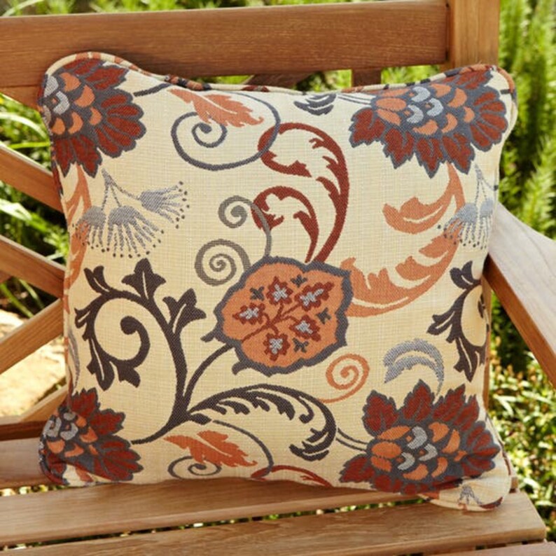 May include: A square throw pillow with a cream background and a floral pattern in shades of orange, brown, and blue. The pillow has a slightly rounded shape and a subtle texture.