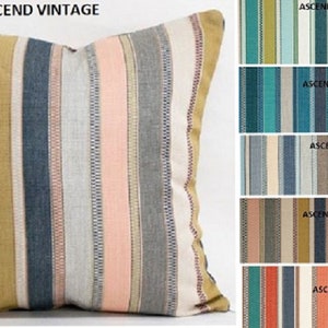 May include: A striped throw pillow with a variety of colors, including pink, blue, gray, and yellow. The pillow is made of a soft, woven fabric and has a subtle sheen. The pillow is shown against a white background.