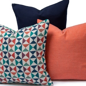 May include: Three decorative throw pillows. One pillow has a geometric pattern with red, blue, green, and white triangles. One pillow is a solid coral color. One pillow is a solid navy blue color.