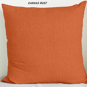 May include: A solid rust orange throw pillow with a smooth, slightly textured fabric. The pillow is square and has a simple, modern design.
