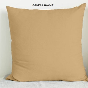 May include: A plain, light brown throw pillow with the text "CANVAS WHEAT" printed on the top.