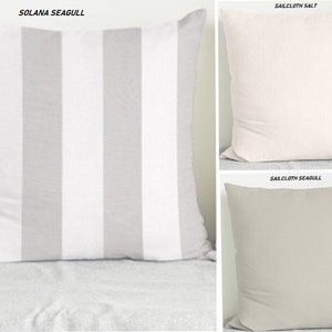 May include: Three decorative throw pillows with different patterns. The first pillow is white with gray stripes, the second pillow is solid light pink, and the third pillow is solid light gray. The pillows are all made of a soft, textured fabric.