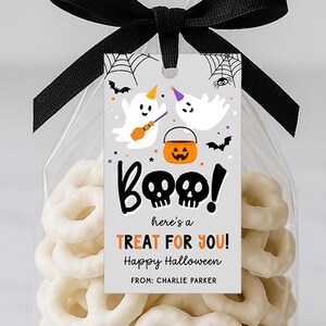 Puede incluir: Una bolsa de regalo con temática de Halloween con un lazo negro y una etiqueta decorativa. La etiqueta presenta fantasmas de dibujos animados, murciélagos y un cubo de calabaza. El texto en la etiqueta dice "¡Boo! ¡Aquí hay un REGALO PARA TI! Feliz Halloween."