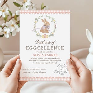 Puede incluir: Un certificado con el texto "Certificate of EGGCELLENCE" y una ilustración de un conejo. El certificado se presenta a "OLIVIA PARKER" y lo otorga "The Easter Bunny". El certificado tiene un borde rosa y lo sostiene una persona.