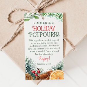 Op de afbeelding: Een wit cadeau-etiket met groene en rode tekst die "Simmering Holiday Potpourri" luidt. Het etiket bevat instructies voor het maken van potpourri en bevat een feestelijke illustratie van kaneelstokjes, sinaasappelschijfjes, dennennaalden en bessen.