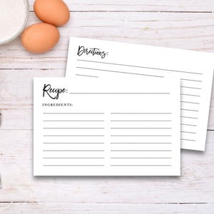May include: Blank recipe card set with lined spaces for writing down ingredients and directions. The card set is on a white wooden background.