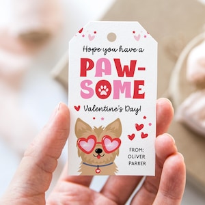 Pode incluir: Uma etiqueta de presente de Dia dos Namorados com um cão de desenho animado usando óculos em forma de coração. A etiqueta diz "Hope you have a PAW-SOME Valentine's Day!" em vermelho e rosa. Pequenos corações e estrelas vermelhas decoram a etiqueta.