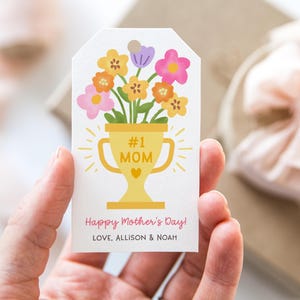 May include: A white gift tag with a yellow trophy design that says "#1 MOM" and a bouquet of flowers. The tag also includes the text "Happy Mother's Day!" and the names "LOVE, ALLISON & NOAH".