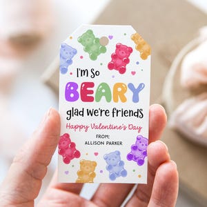 May include: A white gift tag with colorful gummy bear illustrations and the text "I'm so BEARY glad we're friends Happy Valentine's Day". The tag is decorated with hearts and dots.