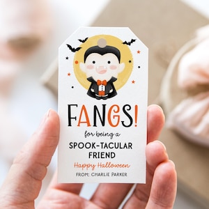 May include: A white Halloween gift tag with a cartoon vampire illustration. The tag reads "FANGS! for being a SPOOK-TACULAR FRIEND Happy Halloween FROM: CHARLIE PARKER" with bats and stars.