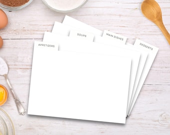 Op de afbeelding: Vijf witte receptverdelers met tabbladen met de labels "Voorgerechten", "Soepen", "Hoofdgerechten" en "Desserts". De verdelers liggen op een wit houten oppervlak.