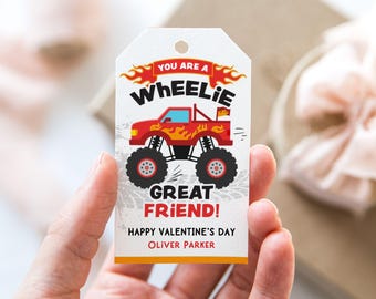 Puede incluir: Una etiqueta de regalo blanca con un diseño de camión monstruo rojo y el texto "YOU ARE A WHEELIE GREAT FRIEND!" en negro y rojo. La etiqueta también incluye "HAPPY VALENTINE'S DAY" y un nombre. La etiqueta tiene un agujero en la parte superior.