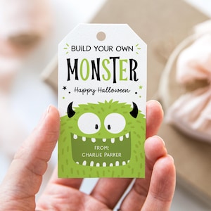 May include: A white tag with a green monster illustration and the text "BUILD YOUR OWN MONSTER" and "Happy Halloween." The monster is green with black horns and a wide grin. The tag includes the text "FROM: CHARLIE PARKER."