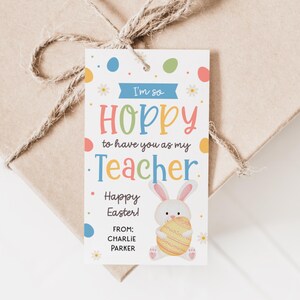 May include: A gift tag with the text "I'm so HOPPY to have you as my Teacher Happy Easter!" and the name "Charlie Parker". The tag features a cartoon bunny holding an Easter egg, with colorful dots and flowers.