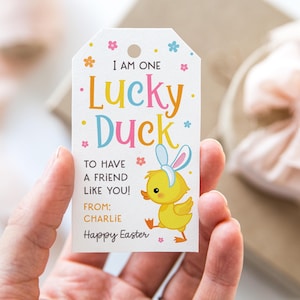 May include: A white gift tag with the text "I AM ONE Lucky Duck" in colorful letters. A cartoon duckling wearing bunny ears is featured. The tag also includes the text "TO HAVE A FRIEND LIKE YOU!" and "Happy Easter".