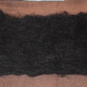 May include: A dark, fluffy mass of black fiber, likely wool or a similar material, rests on a brown surface. The texture appears soft and dense, suggesting it could be used for crafting or textile projects.