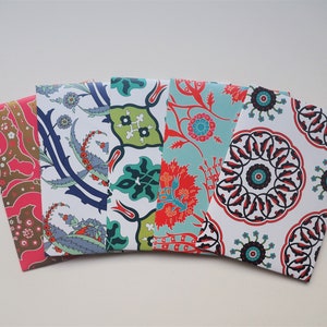 Può includere: Cinque buste di carta decorative con motivi floreali e geometrici colorati. I disegni includono elementi rossi, blu, verdi e marroni su sfondo bianco. Le buste sono disposte a ventaglio.