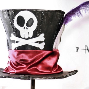 May include: A black top hat with a white skull and crossbones design, a red satin band, and a purple feather. The text "DR. FACILIER" is visible on the right side of the image.