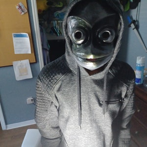 May include: A dark gray hooded sweatshirt with quilted shoulder detailing and a front zipper pocket, paired with a glossy black mask featuring large, circular eye openings and a wide, horizontal mouth slit that covers the entire face.