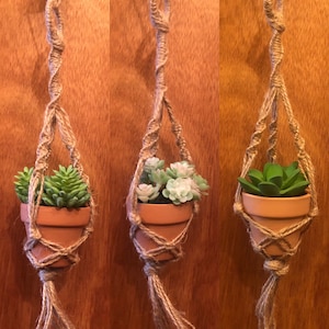 May include: Three macrame plant hangers with terracotta pots and artificial succulents. The hangers are made of natural twine and have a knotted design. The succulents are green and white.