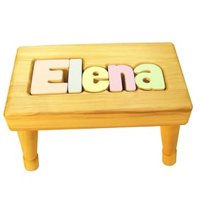 Op de afbeelding: Een houten opstapje met de naam "Elena" gespeld in kleurrijke letters op de bovenkant.