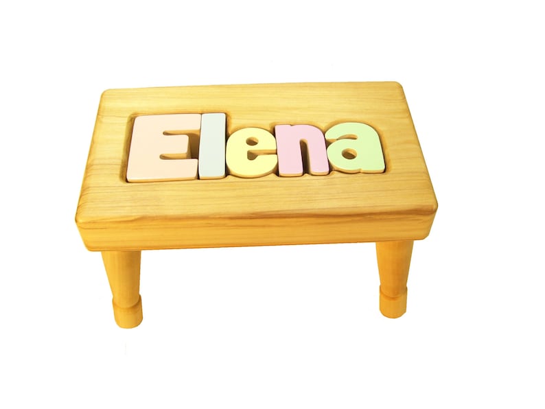 Op de afbeelding: Een houten opstapje met de naam "Elena" gespeld in kleurrijke letters op de bovenkant.