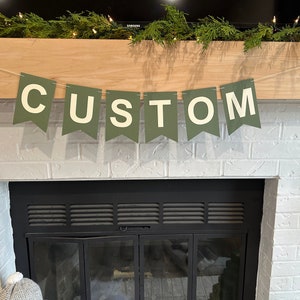 May include: A green banner with white letters spelling "CUSTOM" hanging above a black fireplace with a white brick surround.