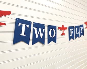 May include: A blue and white banner with the words "TWO TO FLY" and red airplane cutouts.