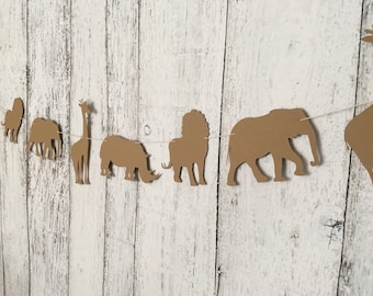 May include: A brown paper garland with cut-out animal shapes, including a giraffe, rhino, lion, elephant, and a monkey. The garland is strung on a white string and is perfect for a safari-themed party.