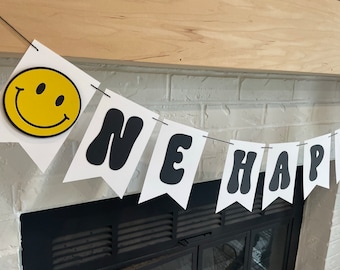 Könnte beinhalten: Weißes Banner mit schwarzen Buchstaben, die "ONE HAPPY" buchstabieren, mit einem gelben Smiley auf der linken Seite.
