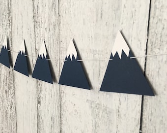May include: A navy blue and white mountain-shaped paper garland with a string for hanging. The garland is made of paper triangles with white snow peaks.