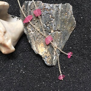Op de afbeelding: Een zilveren ketting met roze edelsteen hangers. De ketting heeft vier roze stenen in verschillende maten en vormen.