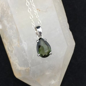 May include: A silver chain necklace with a pear-shaped green gemstone pendant.