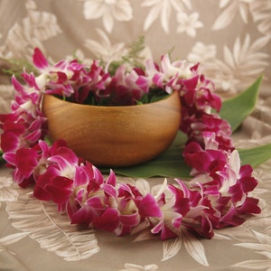 May include: A pink and white orchid lei with a wooden bowl in the background.