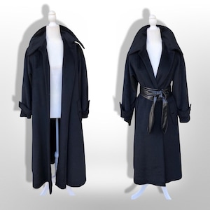 May include: A long black coat with a wide collar and cuffed sleeves, displayed on a mannequin. The coat is shown in two configurations: one open and one cinched at the waist with a black faux leather tie belt, highlighting the versatile silhouette.