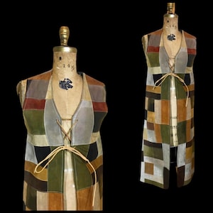 Può includere: Un gilet lungo senza maniche realizzato con toppe rettangolari di pelle scamosciata in varie tonalità della terra, tra cui verde oliva, marrone, beige, grigio e nero. Il capo presenta un profondo scollo a V con chiusura a laccio in pelle.