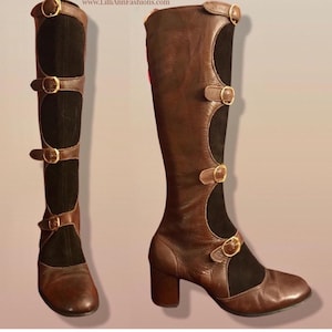 May include: Brown leather knee-high boots with black suede panels and gold-tone buckles. The boots have a block heel and a unique design with cutouts and decorative straps. The boots are a vintage style.