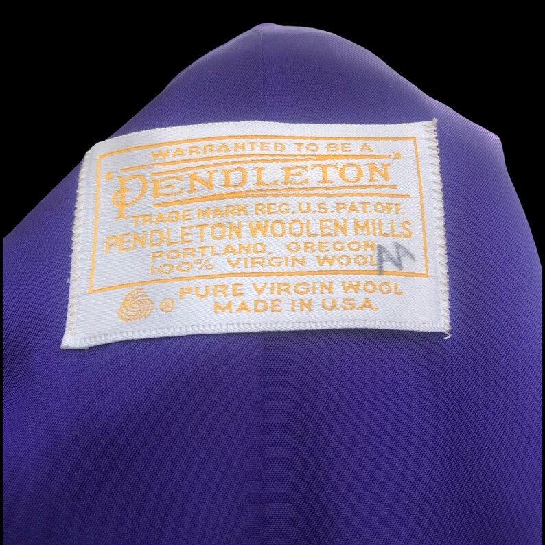 May include: A close-up of a purple garment with a white label. The label, with gold text, reads "PENDLETON WOOLEN MILLS, PORTLAND, OREGON, PURE VIRGIN WOOL, MADE IN U.S.A."