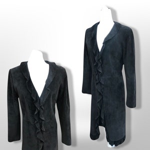 May include: A dark gray long coat with a ruffled front detail. The coat has long sleeves and a collar. The coat is displayed on a white mannequin. The coat appears to be made of a soft, suede-like material.