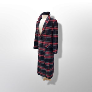May include: A long, plaid coat in black, red, and white, displayed on a mannequin. The coat features a double-breasted design, a wide collar, and two front pockets. The plaid pattern is a classic design.