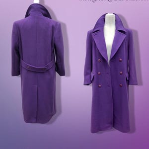 May include: A long, purple coat with a double-breasted design and a wide collar. The coat features a belt at the waist and is displayed on a mannequin. The coat is a solid colour and appears to be made of a wool or wool-blend fabric.