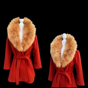 May include: A red coat with a large, tan faux fur collar and a matching belt. The coat is displayed on a white mannequin against a black background. The coat has long sleeves and a wrap-style closure.