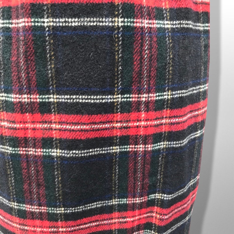 May include: Close-up of a fabric with a classic plaid pattern. The design features a grid of intersecting lines in red, black, white, green, and blue. The fabric has a textured appearance.
