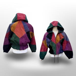 May include: A hooded jacket featuring a multi-colored patchwork design in shades of red, green, purple, black, and mustard yellow. The jacket has a front zipper closure, a drawstring hood, and an elasticized waistband with a gathered hemline.