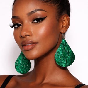 May include: A pair of teardrop-shaped earrings featuring a vibrant green, textured snakeskin-like pattern. These dangling earrings have a metallic sheen and are suspended from silver-toned hooks, providing a bold and eye-catching accessory design.