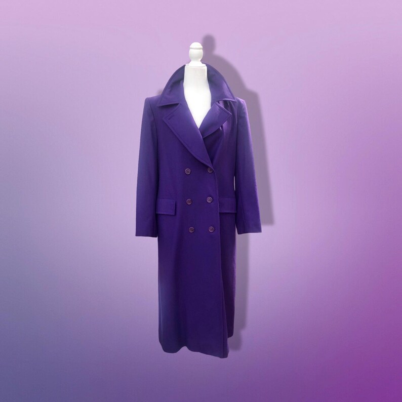 May include: A long, double-breasted purple coat with a wide collar and two rows of buttons. The coat is displayed on a white mannequin against a gradient purple background. The coat has two front pockets.